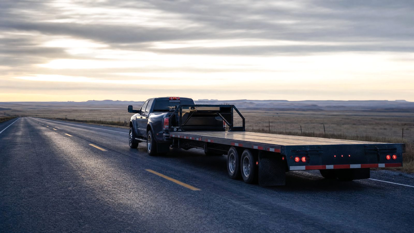 Dually pickup pulling an empty gooseneck flatbed on a prairie highway in the morning